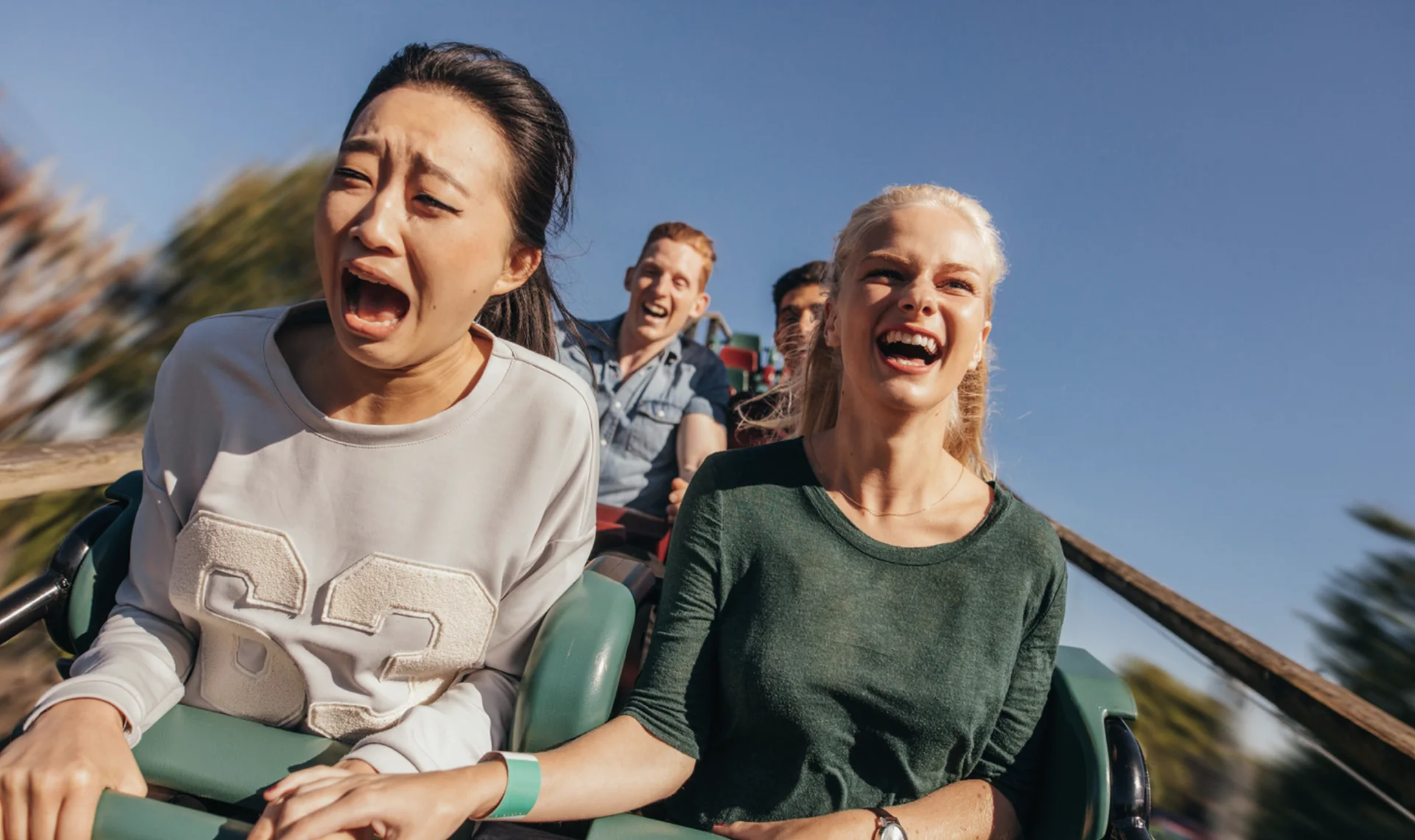 Two women on a roller coaster — one screaming in fear, the other laughing — symbolizing the unpredictability and risk of amusement park rides
