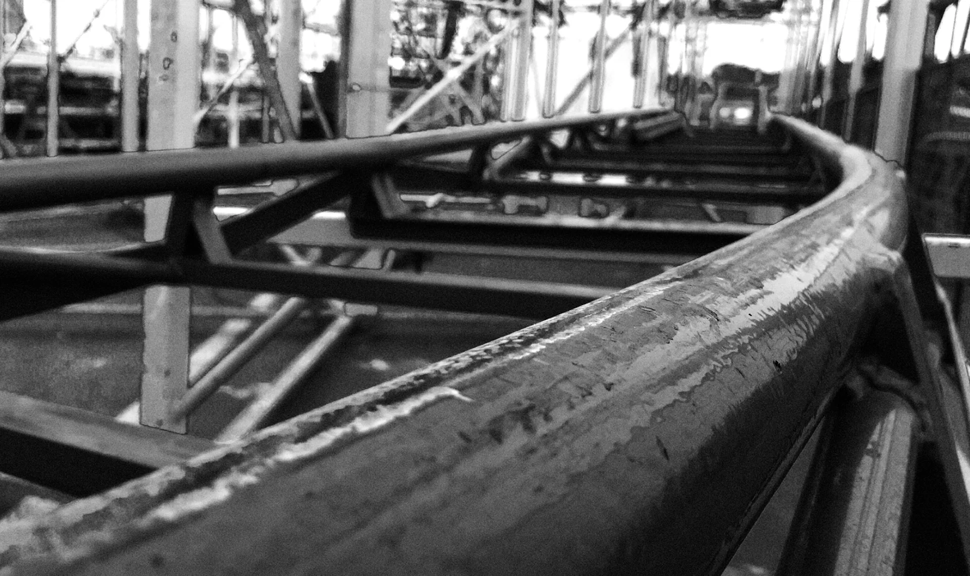 Black and white close-up photo of a steel roller coaster track showing structural beams and a dramatic curve.