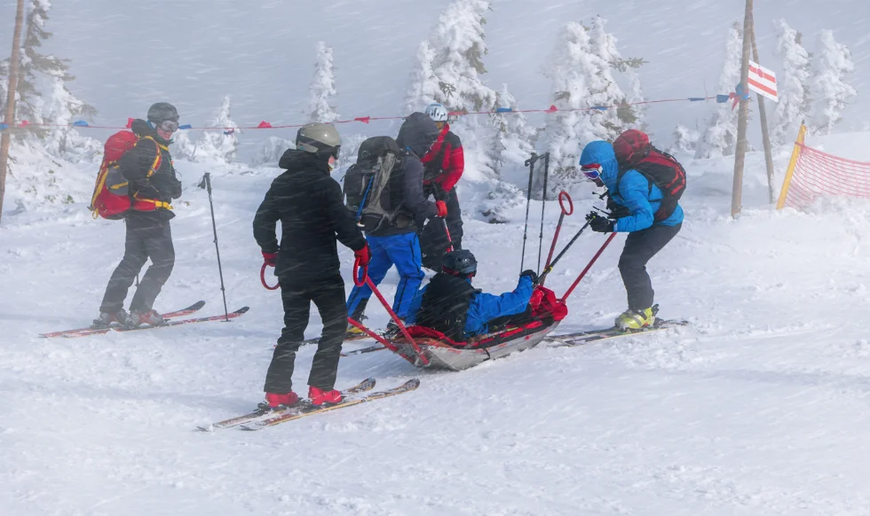 A group of ski patrollers rescuing an injured skier on a snowy slope, highlighting the risks of recreational accidents.