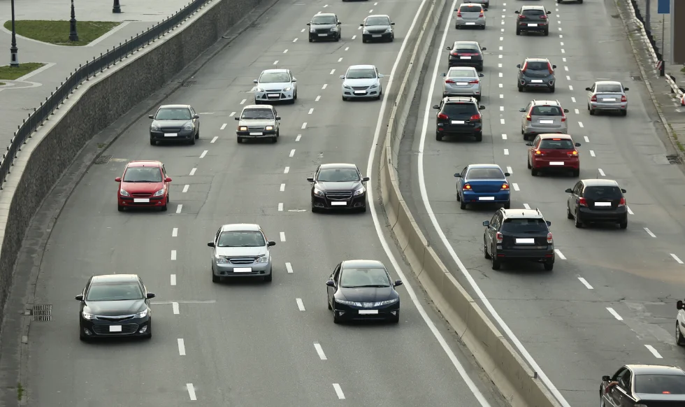 A busy multi-lane highway with cars traveling in both directions, separated by a concrete divider; traffic appears moderate to heavy, suggesting typical commuting conditions.