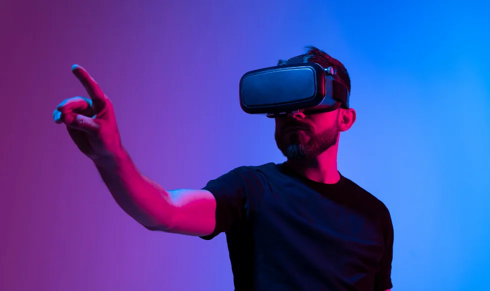 Man wearing a VR headset reaching out in a virtual environment with dramatic blue and pink lighting