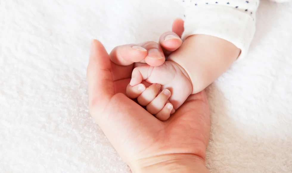 Close-up of an adult hand gently holding a newborn baby’s tiny hand, symbolizing care and protection.
