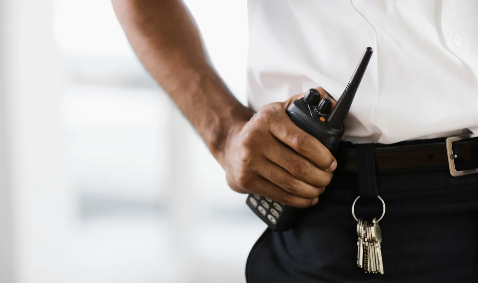 Close-up of a security officer holding a two-way radio with keys attached to their belt, symbolizing premises security and access control.