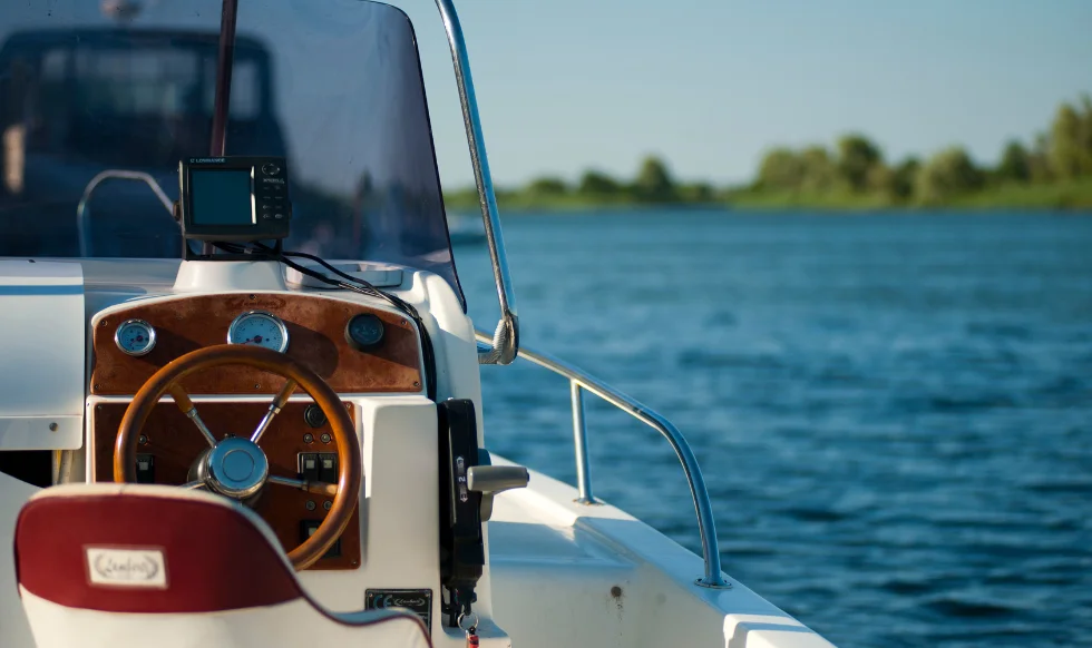 A close-up of a boat's steering console on a lake, with a GPS device and blue water in the background.