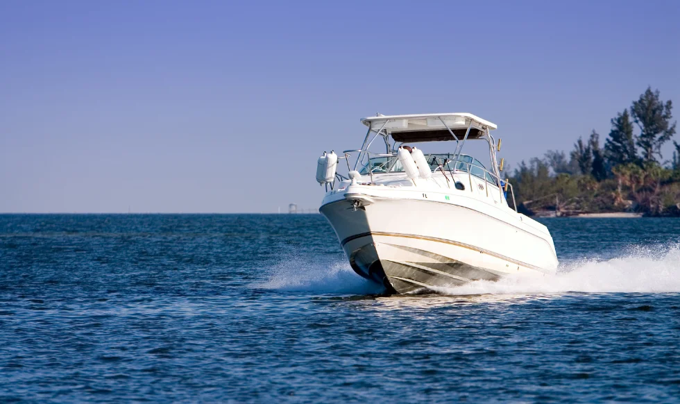 White powerboat speeding through calm blue waters near the shoreline under a clear sky