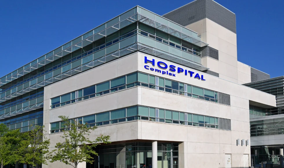 Exterior view of a modern hospital complex with large windows and a blue sky in the background.