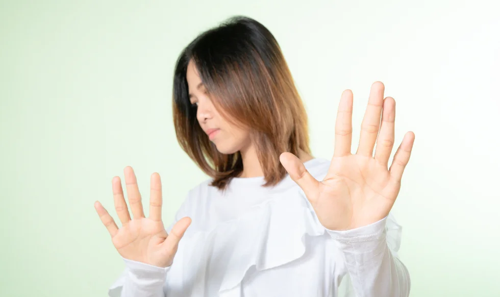 Woman in a white blouse raising both hands to signal refusal, symbolizing declining medical treatment