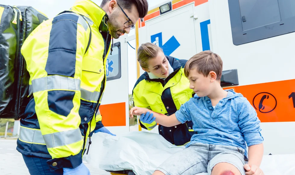Emergency medical responders helping an injured young boy near an ambulance after a car accident.