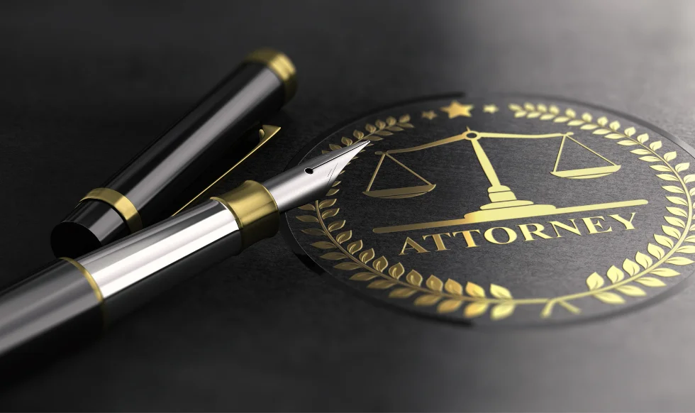 Close-up of a fountain pen resting next to a golden attorney emblem with scales of justice on a dark background