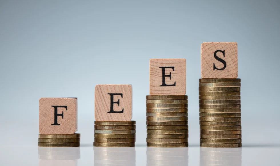 Wooden blocks with letters F, E, E, S placed on increasing stacks of coins, symbolizing rising legal fees or contingency payments.