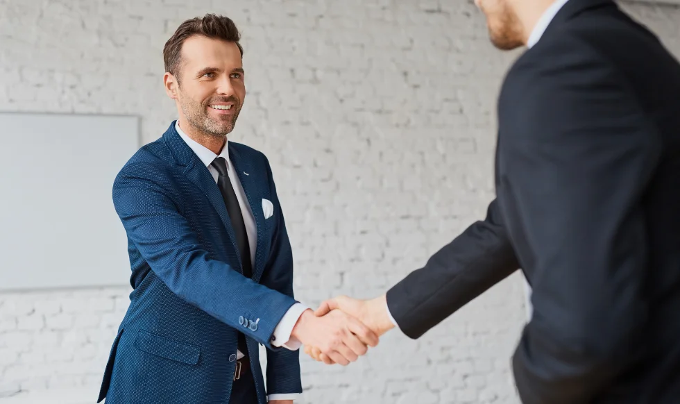 Two professionally dressed men shaking hands in an office setting, symbolizing a successful legal consultation or agreement.